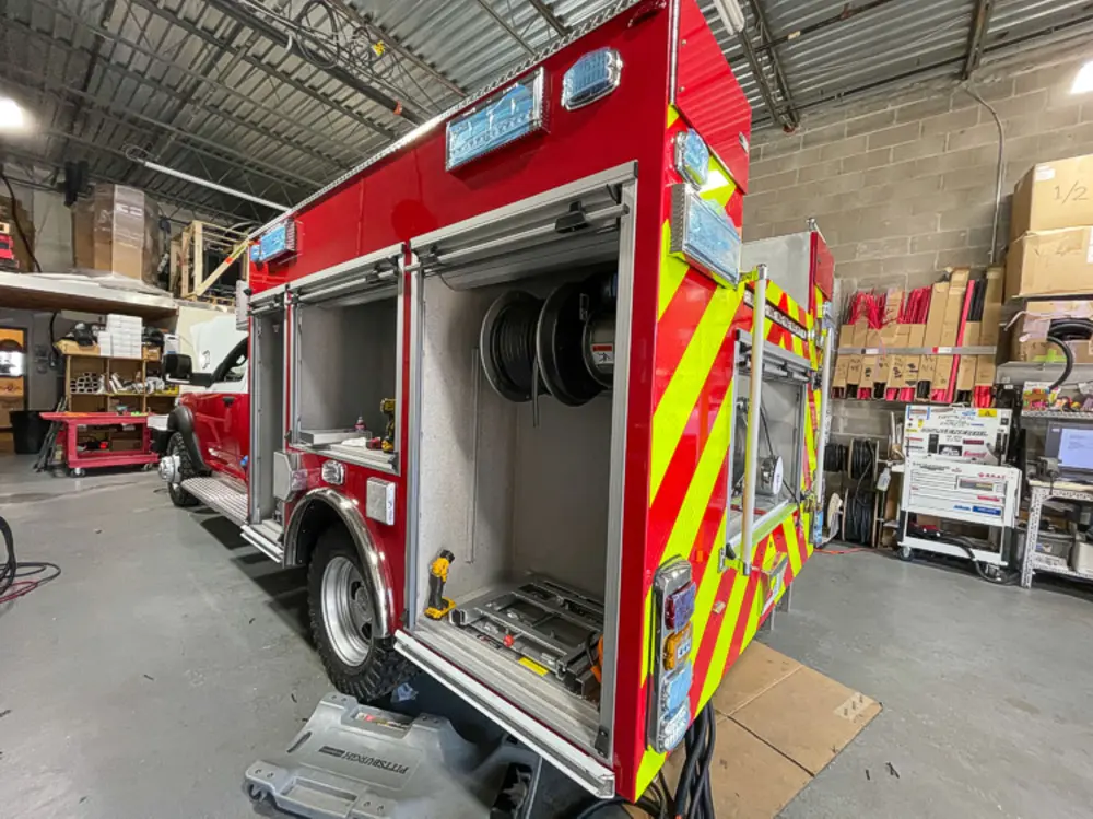 Exterior view of small fire truck showing cab, body compartments, and wheel/tire area.